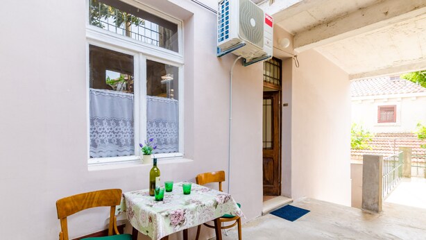 Una habitación pequeña con una mesa y dos sillas, una ventana con cortinas de encaje y un equipo de aire acondicionado en la pared.