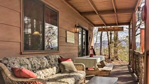 A covered outdoor seating area with a sofa and tables, overlooking a mountainous landscape. - 'Joshua’s Lodge' w/ Hot Tub + Mountain Views! (Franklin)