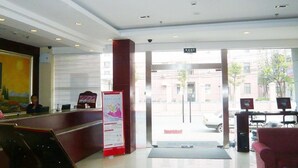 A hotel reception area with a desk, a red couch, and a glass door leading outside. - Hanting Hotel (Shanghai)