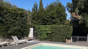 Ein rechteckiger Swimmingpool mit klarem Wasser, umgeben von einer Betonplattform und einem Metallzaun.