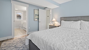 Une chambre à coucher comprenant un lit, une table de chevet, une lampe et une porte donnant sur une salle de bain.