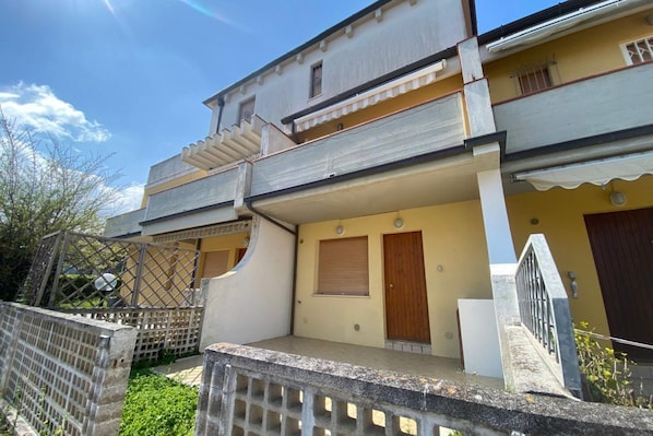 A two-story building with a balcony, a gated entrance, and a small porch area.