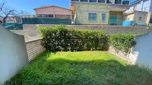 A small, enclosed garden area with a hedge, a concrete wall, and a paved path.