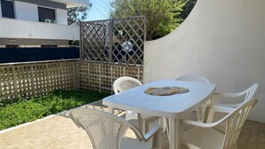 A patio with a white table and chairs, a metal fence, and a white wall.