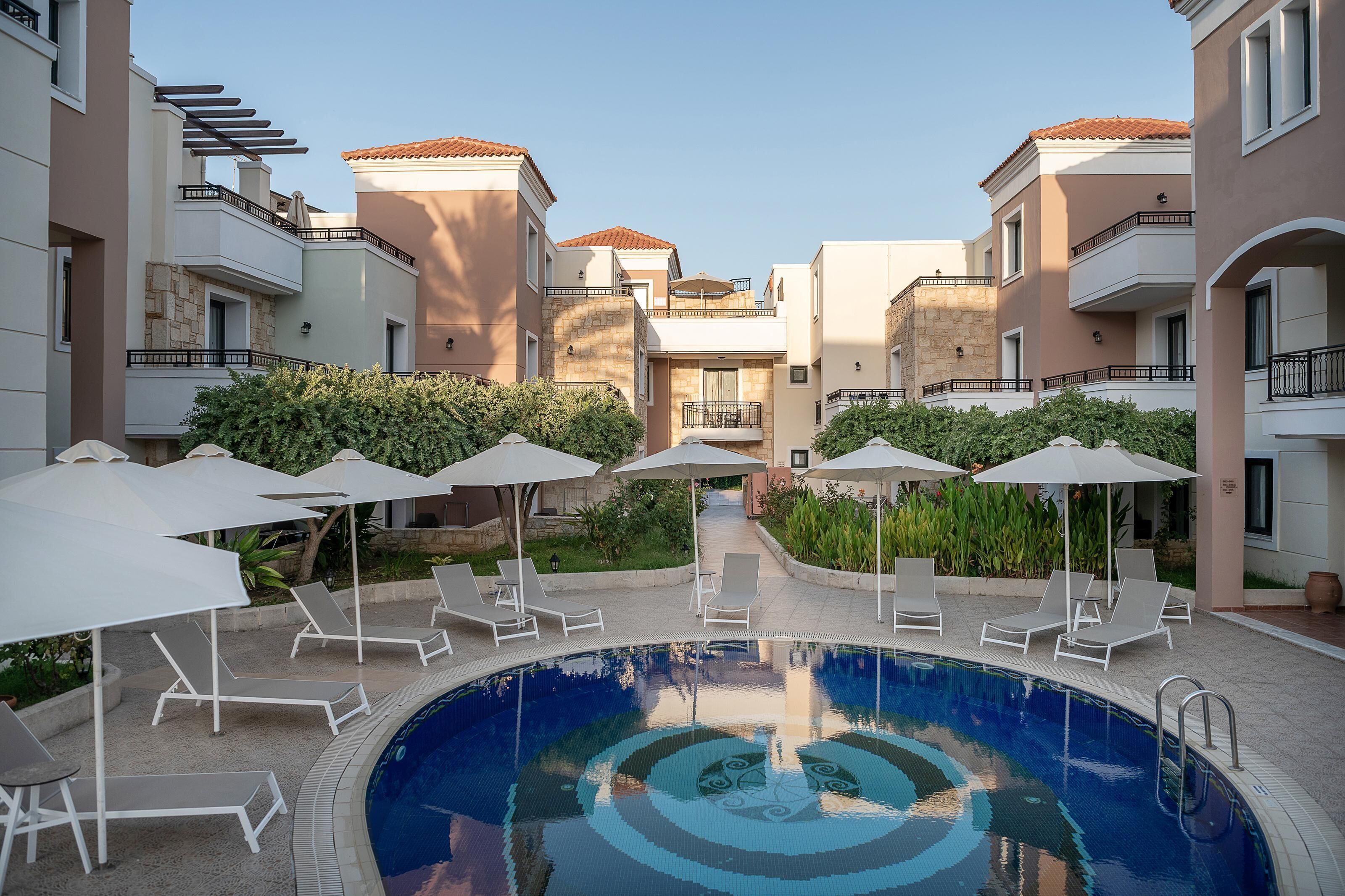 A swimming pool with lounge chairs and umbrellas, surrounded by apartment buildings with balconies.