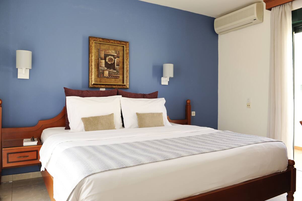 A neatly made bed with white linens and a striped blanket, a wooden headboard, and a framed picture on the wall.