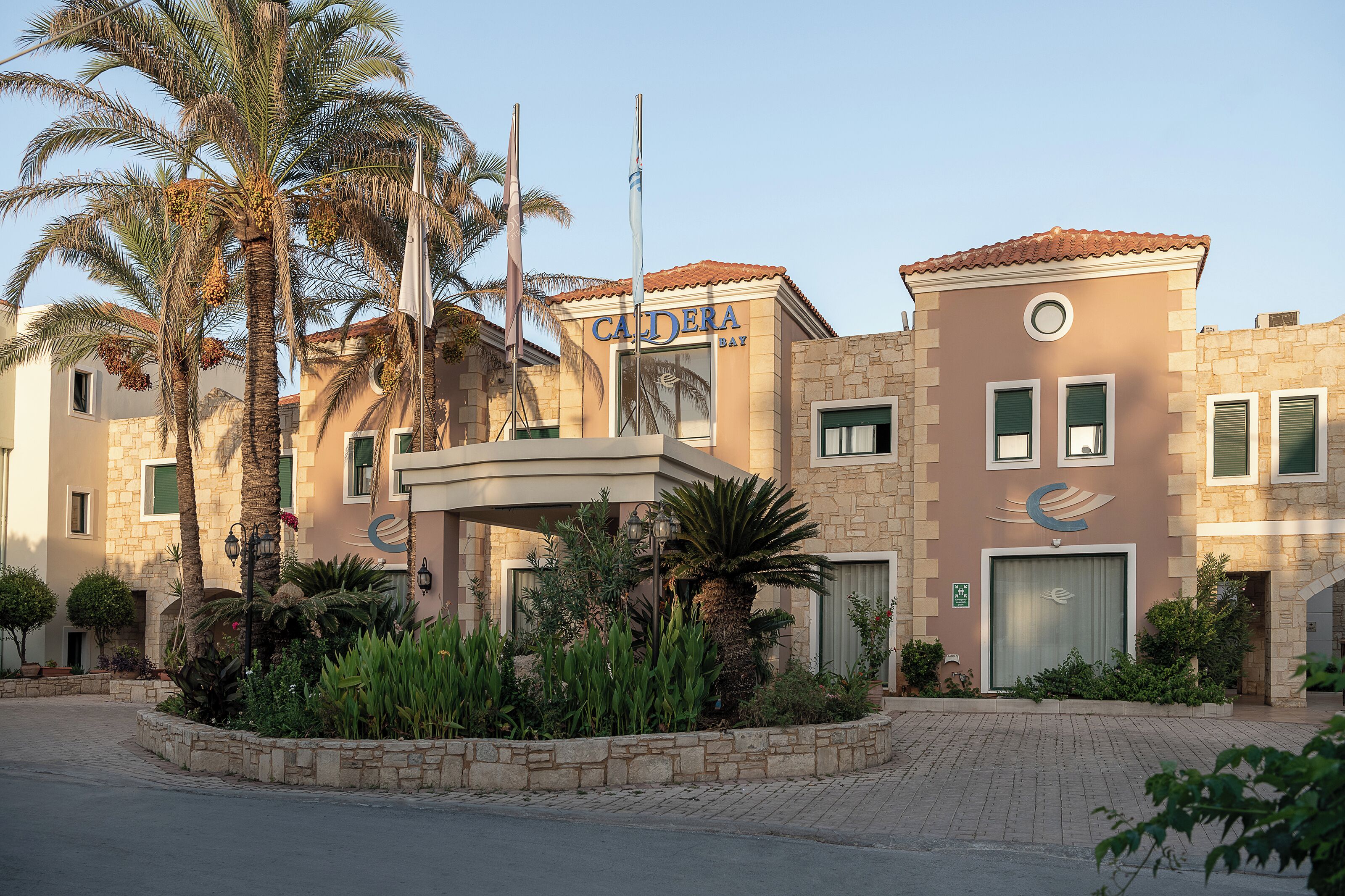 Et hotel med stenfassade, palmetræer og et skilt der siger "CANDERA BAY".