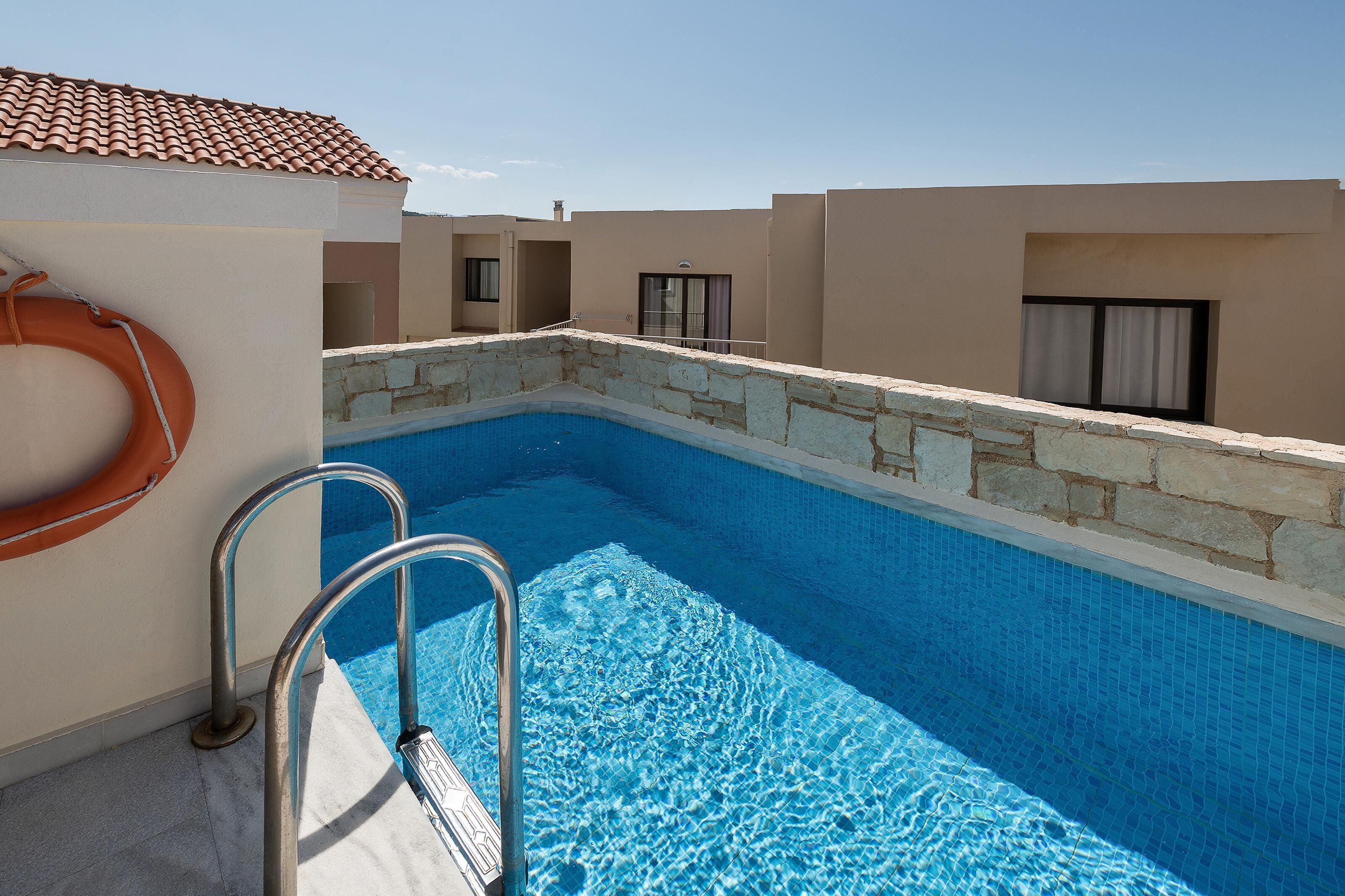A swimming pool with metal ladders, a lifebuoy, and a stone wall.