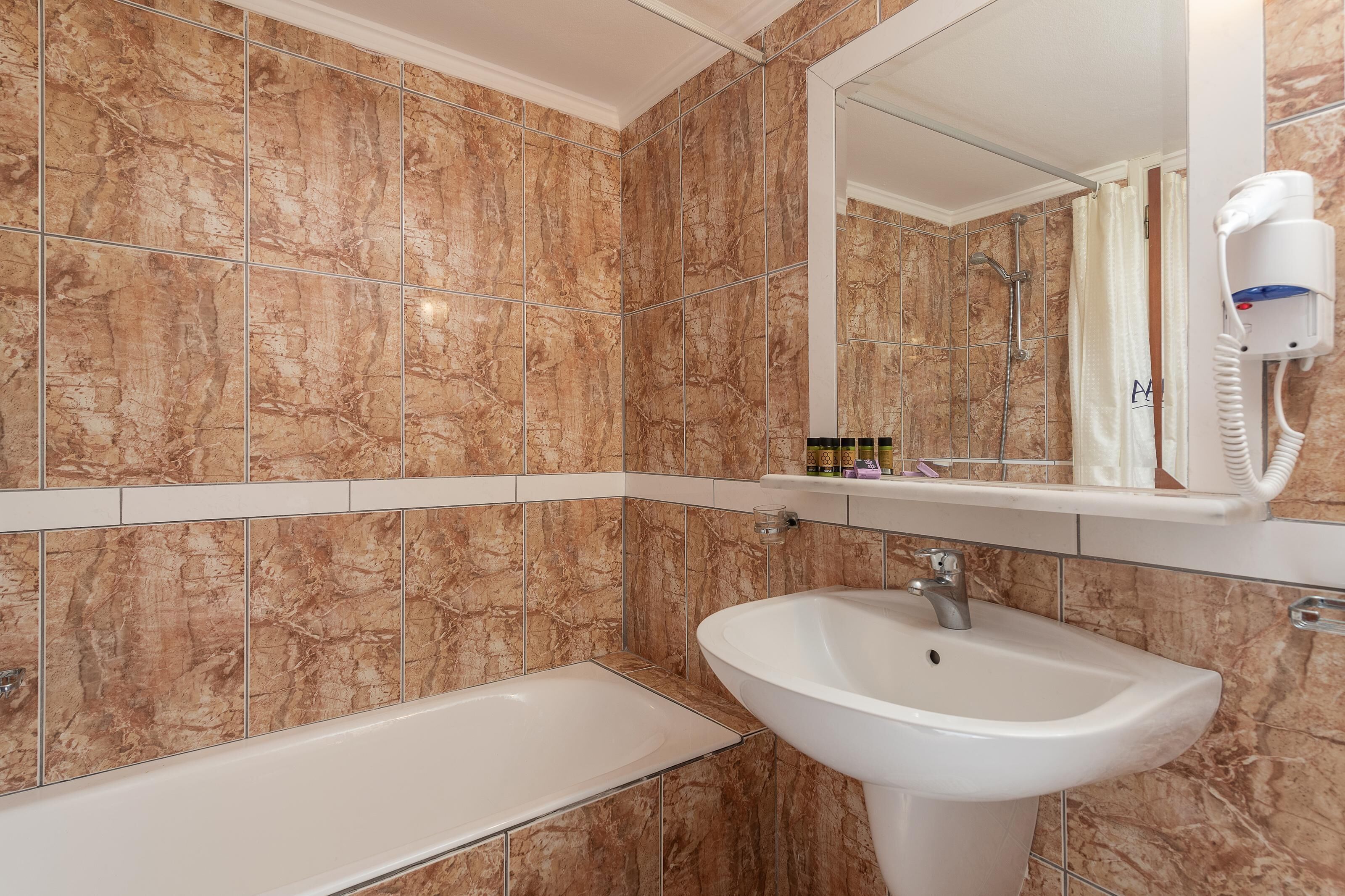 Un baño con pared de azulejos de mármol, lavamanos, espejo y cabezal de ducha de mano.