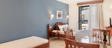 A hotel room with a bed, a small table with chairs, a bedside table with a lamp, and a view of the outside balcony.