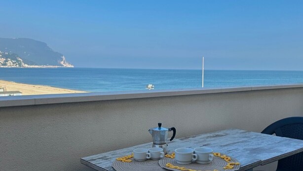 Ein Balkon mit Frühstückstisch, mit Blick auf Strand und Meer.