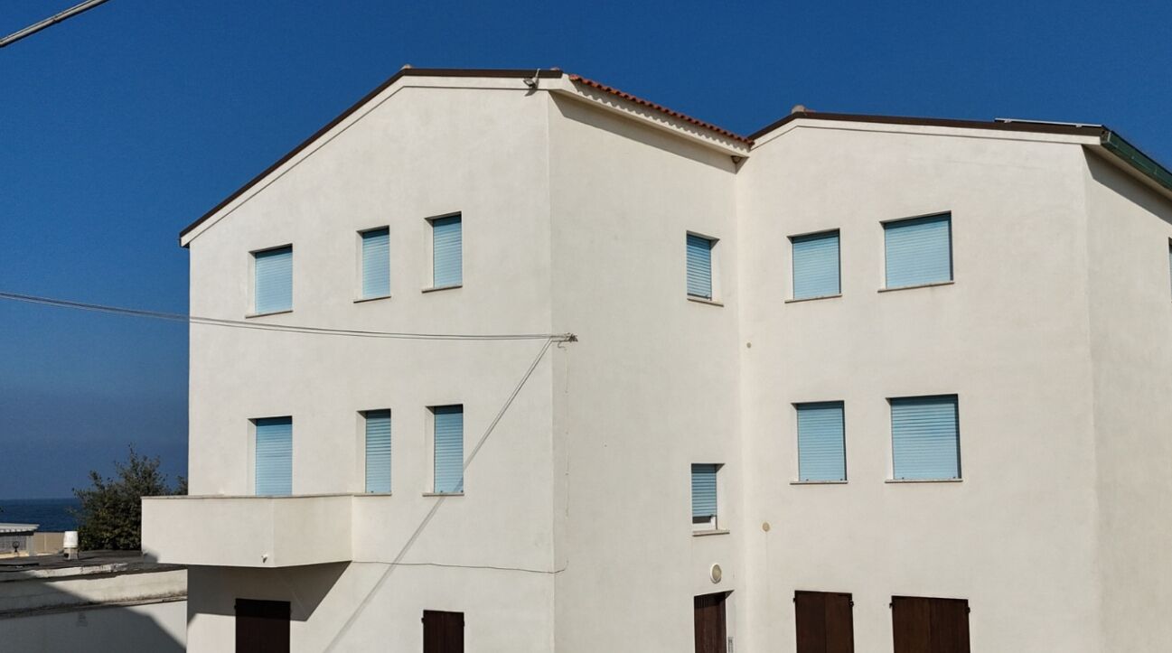 A multi-story building with a flat facade, several windows with shutters, and a visible balcony.