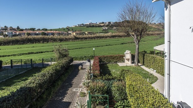 A residential area with a pathway leading to a white building, surrounded by green fields and a clear sky. - M271 - Marcelli, comfortable two-room apartment with balcony (Marcelli)