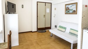 A room with a white sofa, a small table with a television, a door, and a painting on the wall. - M271 - Marcelli, comfortable two-room apartment with balcony (Marcelli)