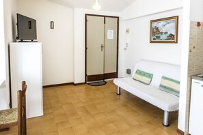 A room with a white sofa, a small table with a television, a door, and a painting on the wall.