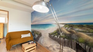 Ett rum med en väggmålning som föreställer en strand, en brun soffa, en trälåda och en golvlampa.