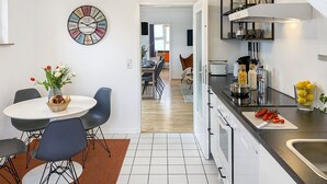Une cuisine moderne avec des meubles blancs, un plan de travail noir et un coin repas comprenant une table ronde et des chaises.