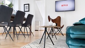 Un salon moderne avec un coin repas, un téléviseur diffusant du contenu de « NETFLIX » et une grande fenêtre.