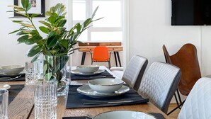Une table à manger dressée avec de la vaisselle transparente, un saladier et des couverts, agrémentée d’une plante et d’une photo encadrée accrochée au mur.
