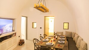 Comedor con una larga mesa dispuesta para una comida, un televisor a la izquierda y un sofá a la derecha.