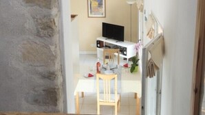Ein Zimmer mit Stehwänden, einer hölzernen Bank, einem weißen Tisch, einem Fernseher und einem Gemälde an der Wand.