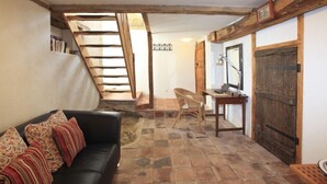 Ein rustikales Interieur mit Steinböden, einer Holztreppe, einem schwarzen Ledersofa und einem Holztisch mit einem Laptop.