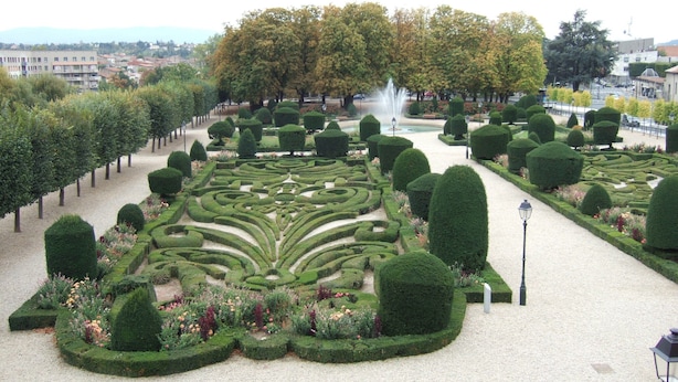 Ein formeller Garten mit geometrischen Hecken, einer Fontäne und einem Weg.