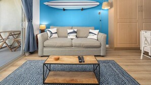 Un salon avec un canapé, une table basse, une planche de surf accrochée au mur et un luminaire suspendu.