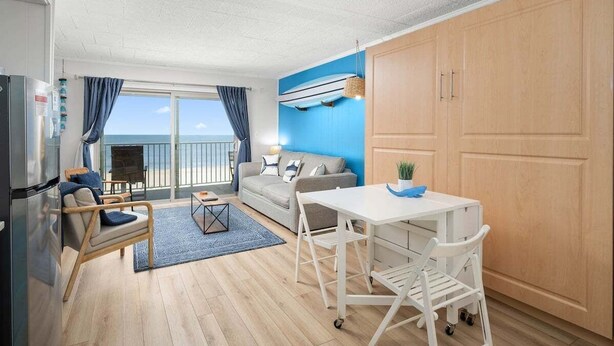 Un espace de vie compact comprenant un coin cuisine, un coin repas et un canapé placé près d’une grande fenêtre donnant sur la mer.