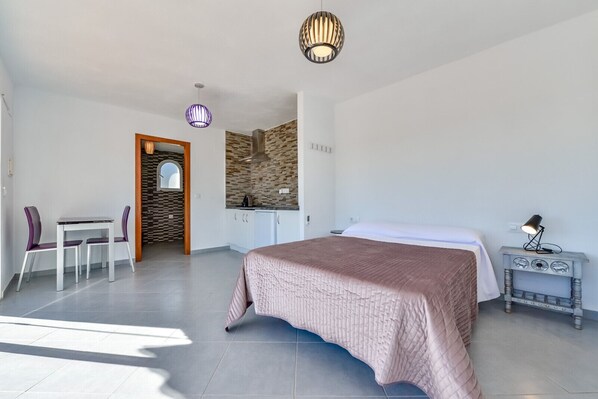 Ein modernes Hotelzimmer mit einem großen Bett, einem Schreibtisch mit zwei Stühlen, einer Küchenzeile und einem Badezimmer mit Dusche.