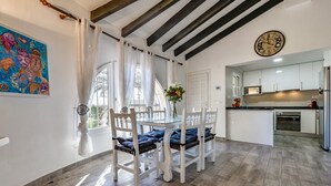 A dining area with a table and chairs, a kitchen with modern appliances, and a clock on the wall. - VILLA MARIA - Villa with sea views and private pool (Calpe)