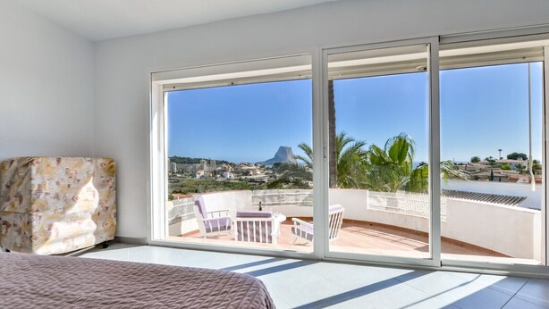 A bedroom with a large sliding glass door leading to a balcony with a view of a mountain and palm trees. - VILLA MARIA - Villa with sea views and private pool (Calpe)