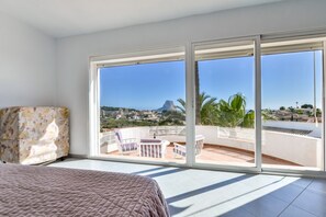 Ein Schlafzimmer mit einer großen SchiebeglasTür, die auf einen Balkon mit Blick auf einen Berg und Palmen führt.