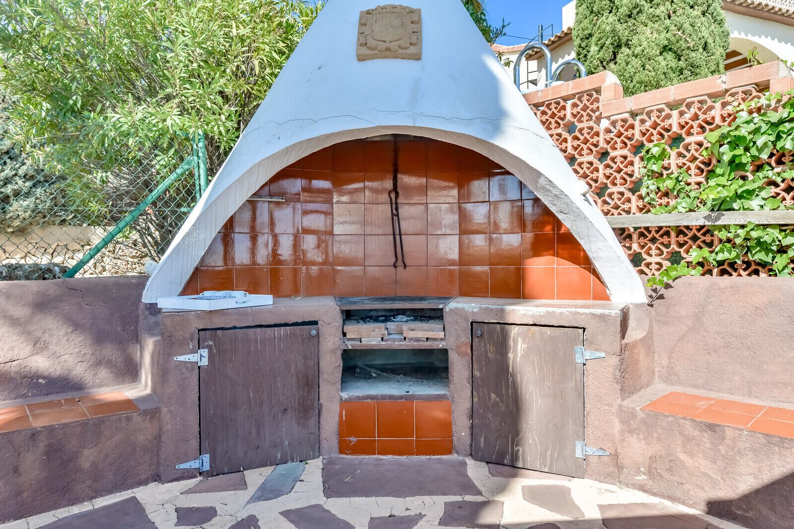 An outdoor brick oven with a white arch and two wooden doors.