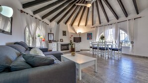 A spacious living area with a high ceiling, a fireplace, a dining set, and a television. - VILLA MARIA - Villa with sea views and private pool (Calpe)
