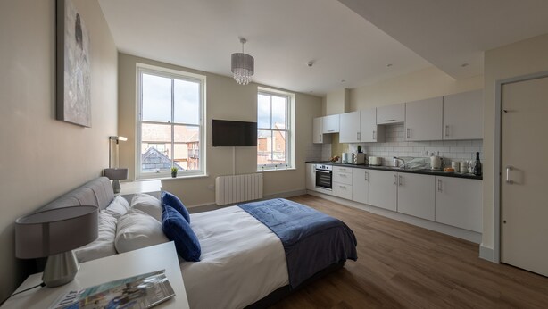 A modern bedroom with a large bed, bedside table, and a TV mounted on the wall. - Apartment 7 Isabella House Hereford (Hereford)