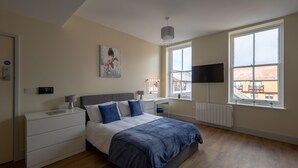 A modern bedroom with a bed, bedside tables, a TV, and a large window. - Apartment 7 Isabella House Hereford (Hereford)