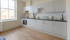 A modern kitchen with white cabinets, a black countertop, and a window providing natural light. - Apartment 7 Isabella House Hereford (Hereford)