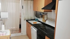 Une cuisine de taille réduite, avec des meubles en bois, une cuisinière noire, un lave-vaisselle blanc et un réfrigérateur.