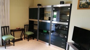 Un espace de vie compact comprenant un coin cuisine, un coin repas avec deux chaises, un téléviseur et un tableau accroché au mur.