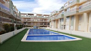 Une piscine entourée d’un gazon artificiel vert, située dans un immeuble à plusieurs étages doté de balcons et de fenêtres.