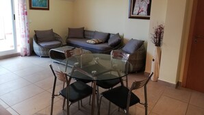 Un salon comprenant un canapé, une table à manger en verre avec des chaises, et deux tableaux encadrés accrochés au mur.
