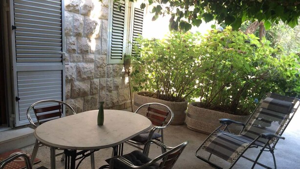 Une terrasse extérieure avec une table ronde et des chaises en métal, entourée de murs en pierre et de plantes en pot.