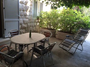 An outdoor patio with a round table and metal chairs, surrounded by stone walls and potted plants. - Green apartment (Sveti Stefan)