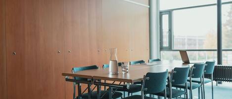 A conference room with a wooden panel wall, a large window, a table with chairs, and a laptop.