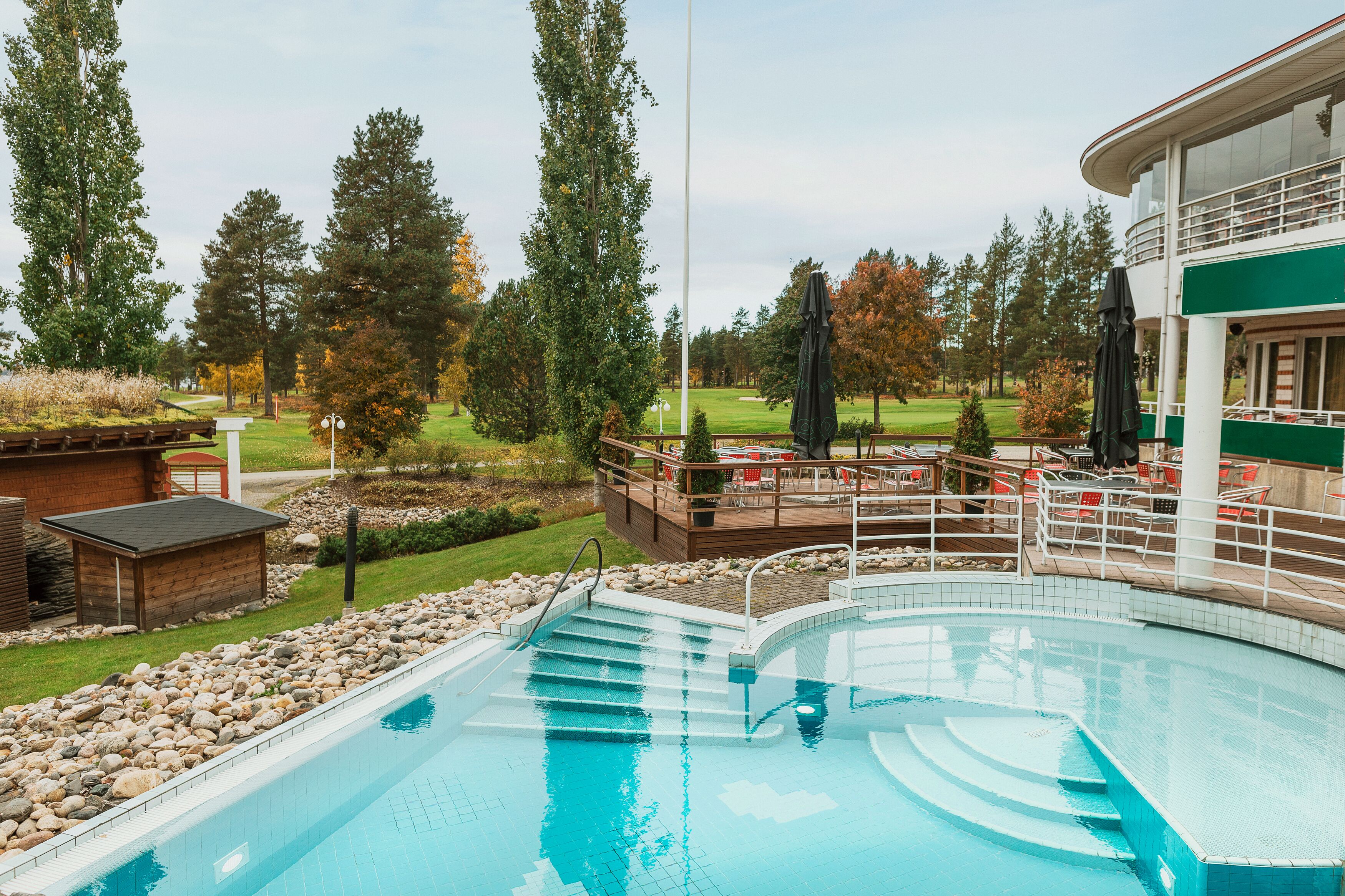A swimming pool with a deck area, surrounded by trees and a golf course in the background.
