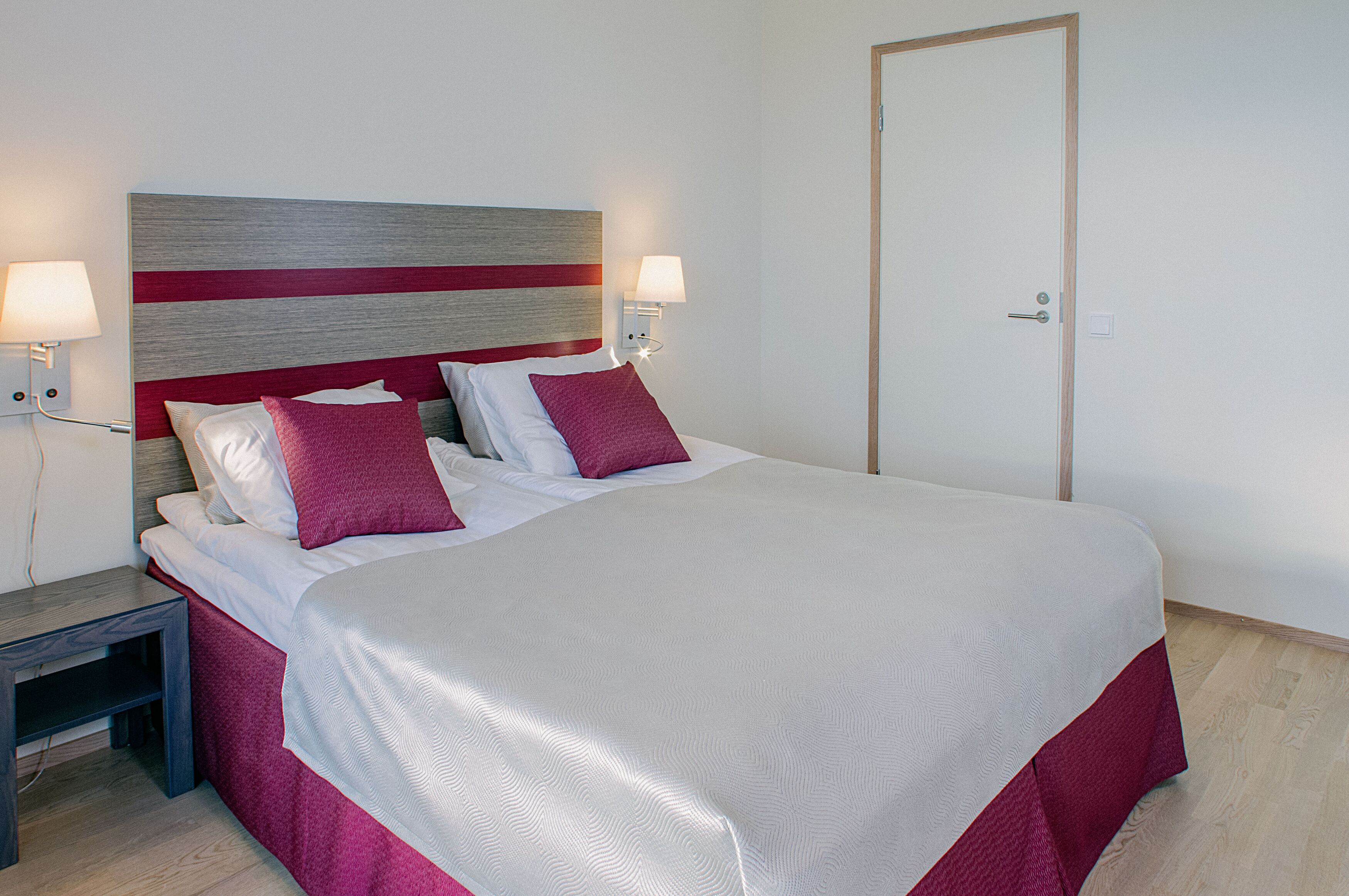 A neatly made bed with a striped headboard, two bedside lamps, and a wooden nightstand.