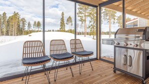Un espace extérieur moderne, aménagé avec des chaises en osier et un coin barbecue doté d’un gril en acier inoxydable.