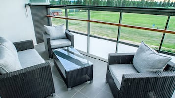 En balkon med fletningsmøbler, et glasbord og udsigt over en græsplæne.