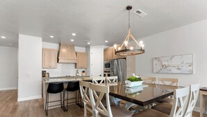 A modern kitchen with wooden cabinets, a central island with bar stools, and a chandelier. - Pirates Den at the Shores: Desert Color Lagoon + Beaches (Saint George)
